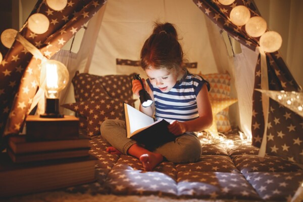Mädchen mit einer Taschenlampe in der Hand liest ein Buch