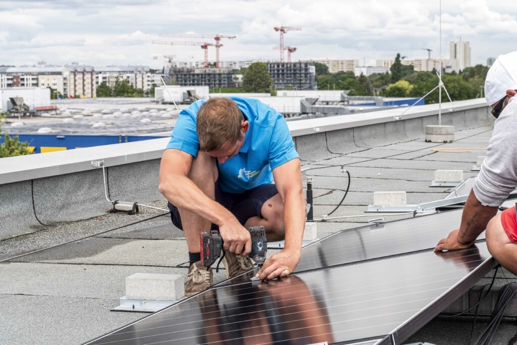 Monteure installieren eine Solaranlage der Berliner Stadtwerke auf einem Dach in der Rhinstraße in Berlin-Lichtenberg