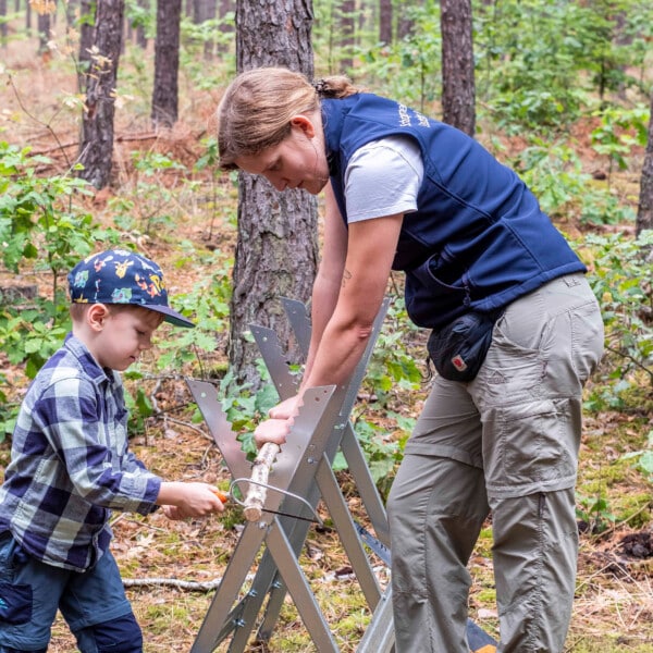 Ein Junge und eine Mitarbeiterin der Schutzgemeinschaft Deutscher Wald sägen an einem Ast