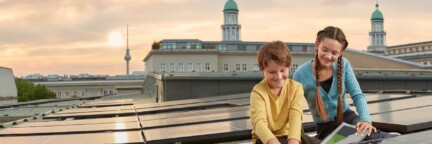 Zwei Kinder befinden sich auf einem Dach mit einer Solaranlage mit Blick auf dem Fernsehturm