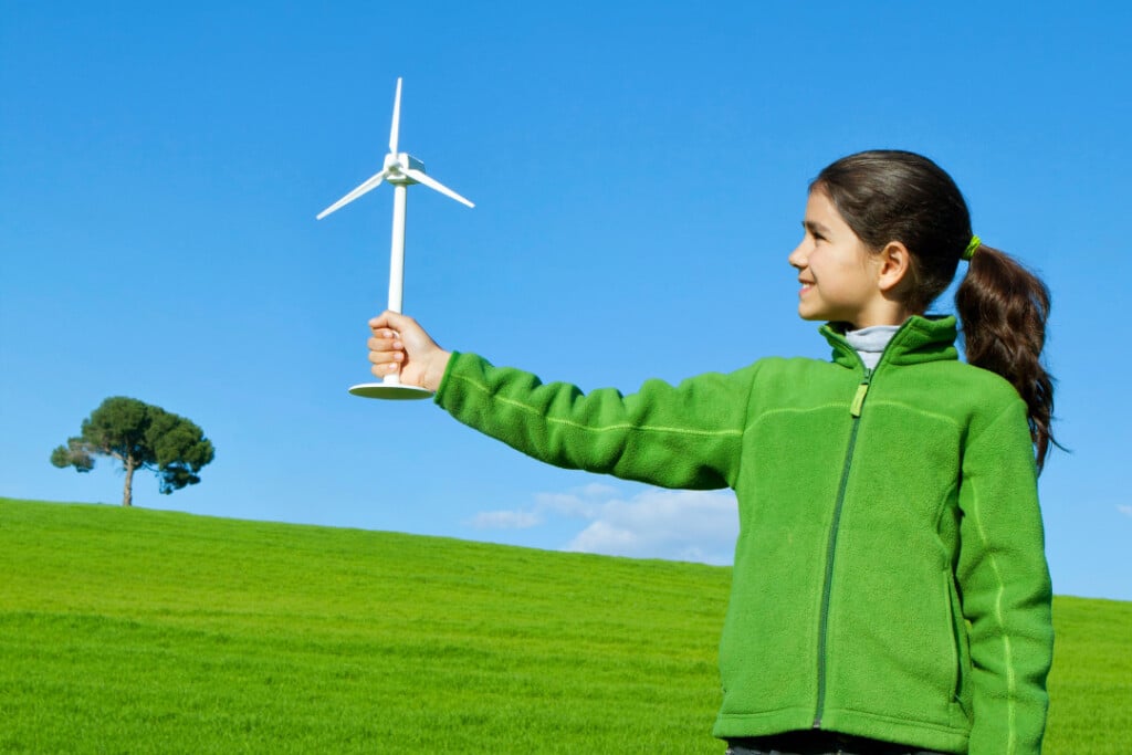 Mädchen mit Modell einer Windenergieanalge in der Hand vor blauem Himmel