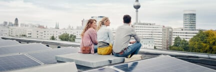 Drei Menschen auf einem Solardach in Berlin mit Blick auf den Fernsehturm