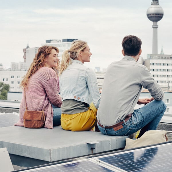 Drei Menschen auf einem Solardach in Berlin mit Blick auf den Fernsehturm