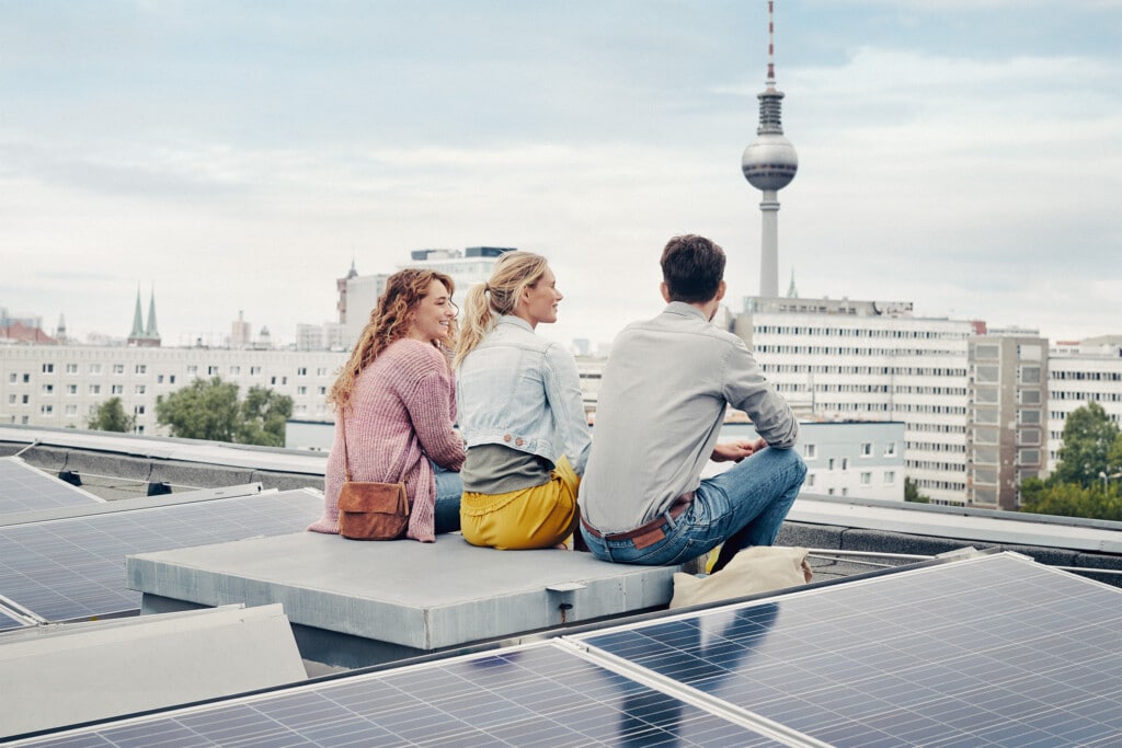 Drei Personen sitzen auf einem Dach in Berlin mit einer Solaranlage mit Blick auf den Fernsehturm