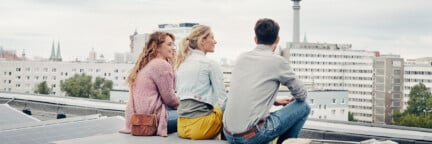Drei Personen sitzen auf einem Dach in Berlin mit einer Solaranlage mit Blick auf den Fernsehturm